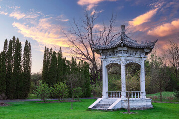 Chinese style stone gazebo in a public park with green lawn and trees in the background