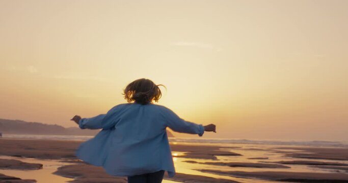 Camera follows happy and carefree woman run barefoot in low tide beach water. Run towards sun and ocean. Dreamy vacation holiday in exotic location