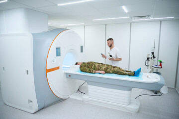 Serious radiographer preparing military man for magnetic resonance imaging exam