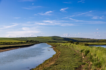 A pathway running alongside the Cuckmere River in the South Downs, with a blue sky overhead