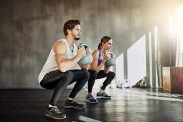 Training, squat and couple in gym with kettlebell, power fitness and workout challenge together at sports club. Man, woman or personal trainer with muscle development, healthy body and exercise.