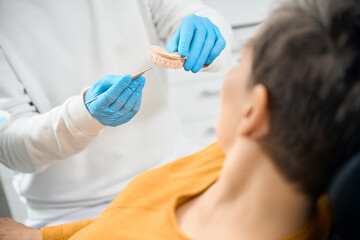Close-up dental therapist showing to female client her problem zone on tooth