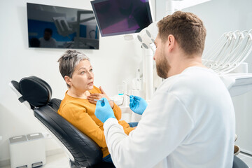 Fototapeta premium Nervous woman afraid of dental examination, doctor undertake check-up carefully