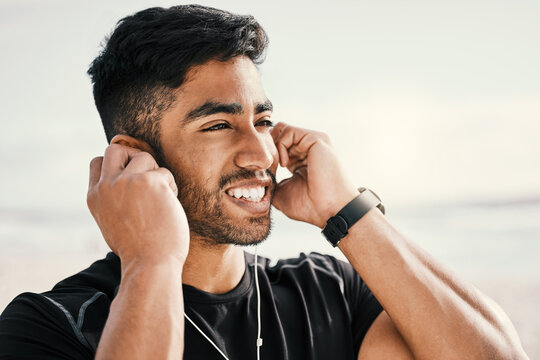 Fitness and happy man and thinking with earphones for listening to music on run or workout at beach. Smile, male person and sports with smartwatch and audio track for streaming and tracking steps