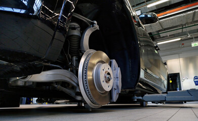 Car in a service station on a lift. The wheel has been removed from the car and we can see the brake disc and brake caliper.