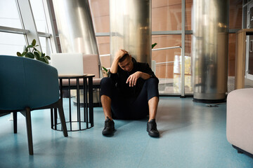 Unhappy guy sitting on floor in coworking center