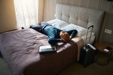 Tired african american businessman lying and resting on bed with open laptop