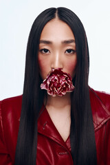 Beautiful woman with long black hair wearing red jacket and flower in mouth