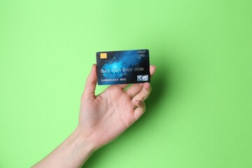 Woman holding credit card on light green background, closeup