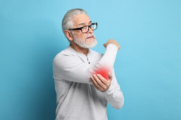 Senior man suffering from pain in elbow on light blue background