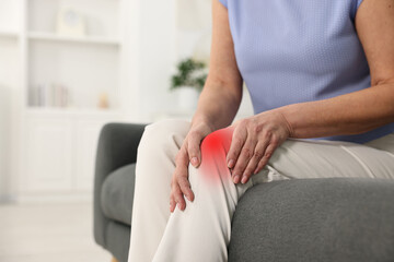 Woman suffering from pain in knee on sofa indoors, closeup