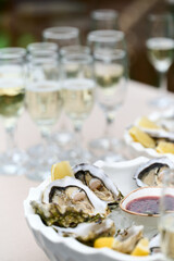 Opened fresh oysters in a plate with red sauce in a plate. In the background, glasses are filled with champagne. Vertical shot