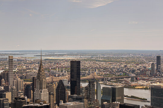 New York, NY, USA - August 2, 2023: Ed Koch Queensboro Bridge over East River partly hidden by Chrysler Building and other skyscrapers as seen from Empire State Building. Wide landscape behind under b - Powered by Adobe