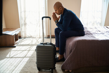 Side view of thoughtful african american male entrepreneur sitting on bed - Powered by Adobe