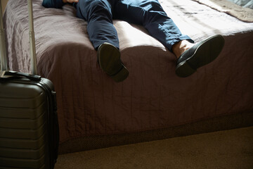Cropped image of tired male entrepreneur lying and resting on bed in hotel room