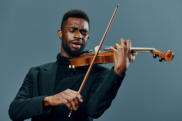 Talented African American man in black suit showcasing his violin skills against a neutral gray...