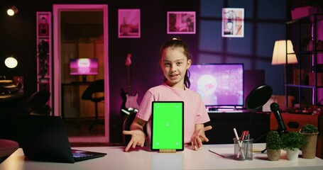 Smiling child in home studio presenting advertisement from sponsoring brand on green screen tablet. Little kid using chroma key device to present promotion from media partner to followers - Powered by Adobe