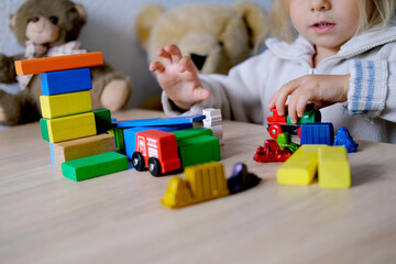 small child, blonde girl 3 years old plays toys, builds towers and buildings from colored wooden...