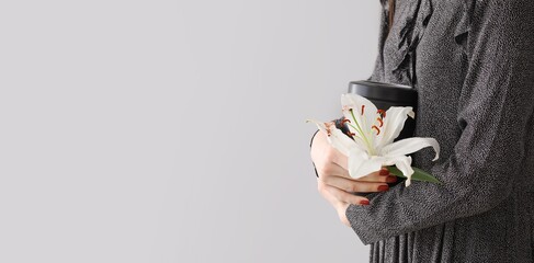 Woman holding mortuary urn and lily flower on light background with space for text. Funeral concept