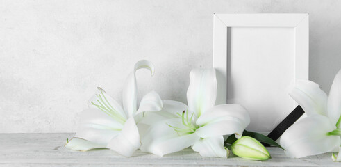 Blank funeral frame and beautiful lily flowers on table