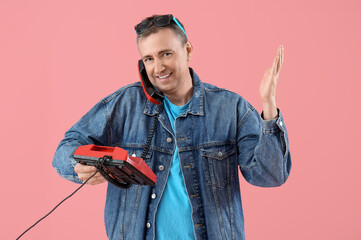 Mature man talking by telephone on pink background