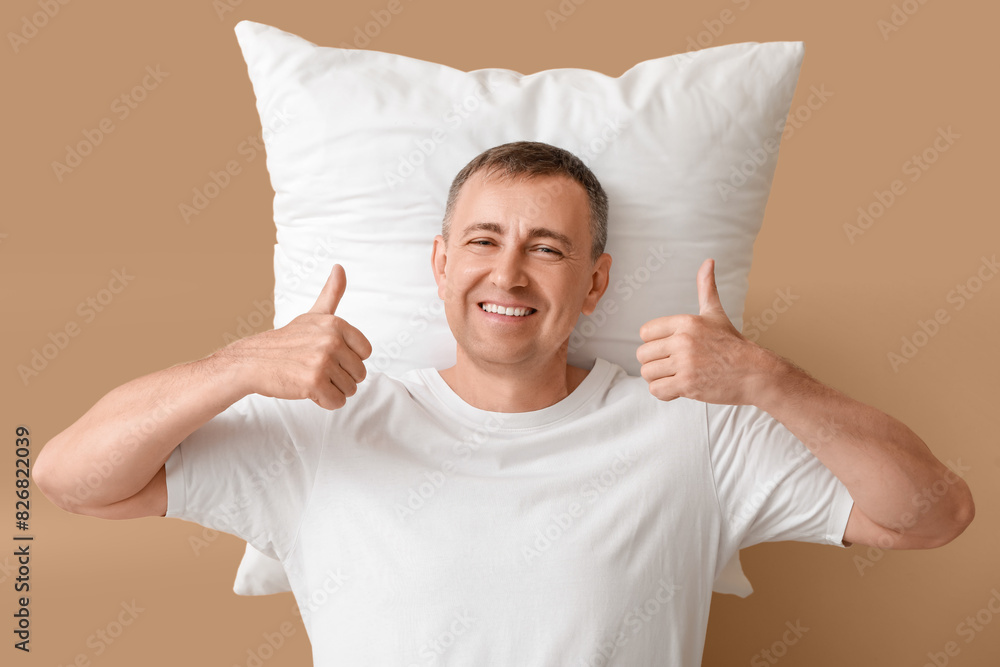 Canvas Prints Mature man with soft pillow showing thumbs-up on beige background