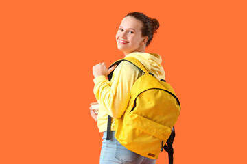 Beautiful young woman in stylish hoodie with backpack and books on orange background