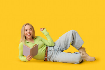 Beautiful young happy woman with book lying on yellow background
