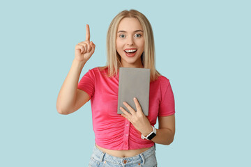 Beautiful young happy woman with book pointing at something on blue background