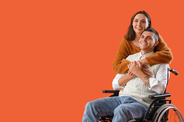 Young man in wheelchair and his wife hugging on orange background
