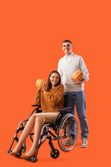 Naklejka premium Young man and his wife in wheelchair with pumpkins on orange background
