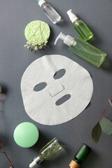 Facial sheet mask with different cosmetic products, gypsophila flowers and leaves on grey background