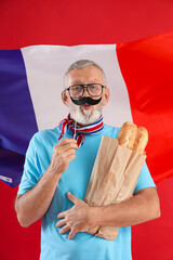 Senior man with paper mustache and baguettes against flag of France on red background