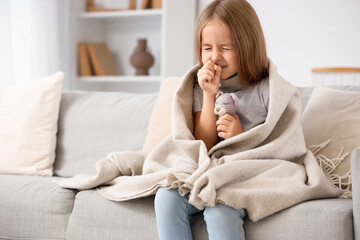 Sick little girl with toy coughing on sofa at home