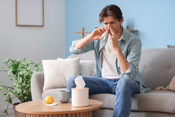 Sick young man using nasal drops on sofa at home