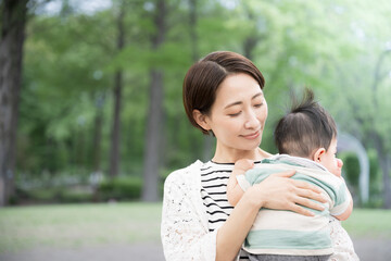 Fototapeta premium 新緑の公園で赤ちゃんを抱く母親 幸せや幸福、見守り、守る母性のイメージ
