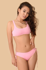 Fototapeta premium Attractive young woman in pink swimsuit on beige background