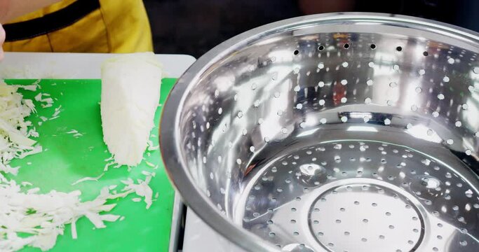Woman's hands take the sliced cabbage and place it in a deep metal container with holes and then wash it with water.