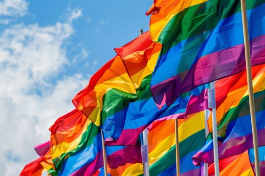 Vibrant collection of rainbow flags fluttering against a blue sky, symbolizing diversity and pride in a celebratory display