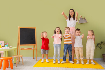 Little children with nursery teacher showing thumbs-up in kindergarten
