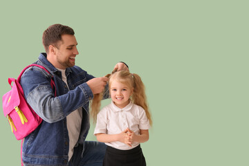 Father doing hair of his cute little schoolgirl on green background
