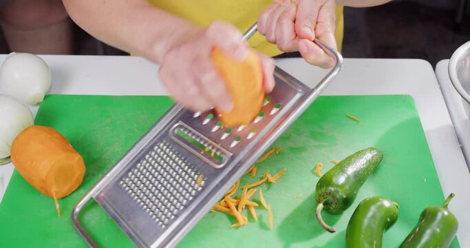 Woman's hands grating carrot and other vegetables.