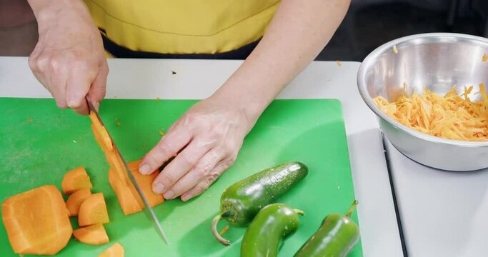 Woman's hands cutting carrot into small pieces.