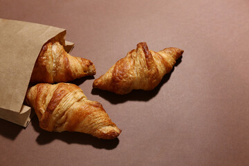 Paper bag with tasty croissants on brown background