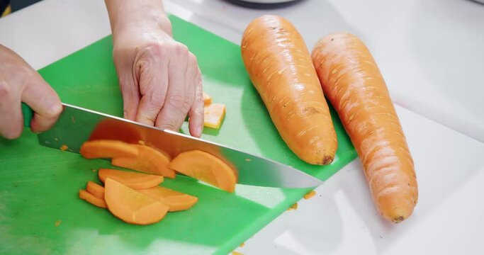 Woman's hands cutting carrot into thin slices.