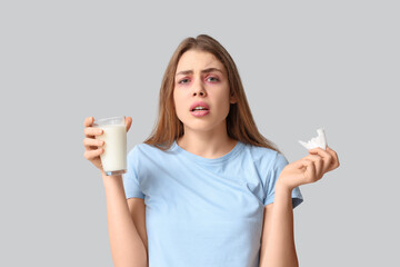 Young woman with glass of milk and tissue suffering from allergy on grey background