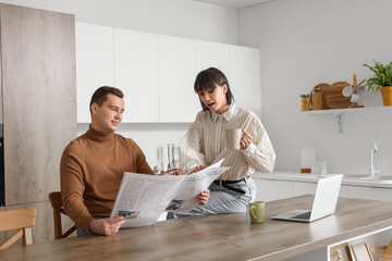 Young loving couple reading newspaper in kitchen