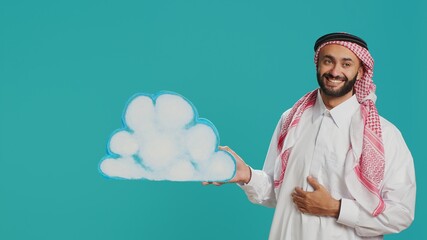 Middle eastern guy presents cloud board in studio, holding isolated billboard cutout in natural...