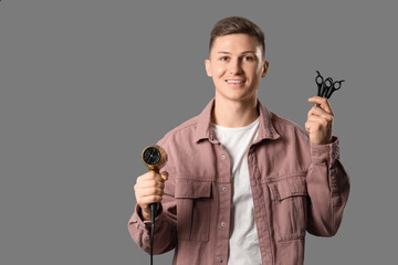 Male barber with hair dryer and scissors on grey background