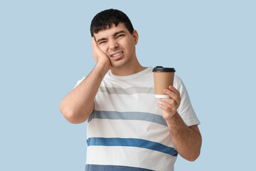 Young man with coffee cup suffering from toothache on blue background